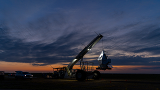 The EXCITE (EXoplanet Climate Infrared TElescope) mission prepares for launch via a scientific balloon in this photograph taken on Aug. 31, 2024, at NASA’s Columbia Scientific Balloon Facility in Fort Sumner, New Mexico.

Credit: NASA/Sophia Roberts

Alt text: A large vehicle hosts a telescope. 

Image description: A large vehicle stands in the center as dawn breaks over a desert landscape. The vehicle has a long arm extending forward. At the end of the arm dangles a shiny silver telescope. The top is conical, and various rectangular structures are attached to the bottoms and sides. The vehicle has lights along the arm that illuminate the telescope. There’s a truck parked to the vehicle’s left. In the distance, the sky is orange at the horizon, shading from purple to blue at the top of the image. There is a line of streaky clouds across the center.